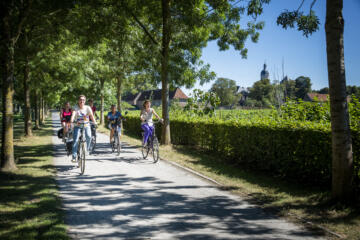 Fietsers langs verharde weg tussen bomen met achteraan zicht op abdij van Vlierbeek.