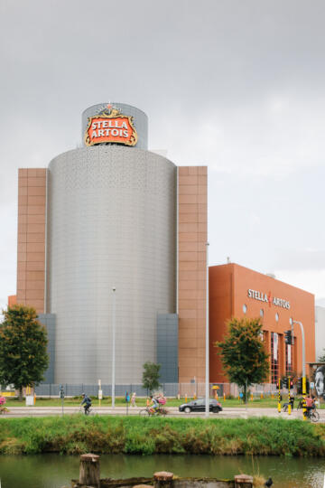 Groot industrieel gebouw met rode en beige bakstenen, glazen ramen en een toren met het Stella Artois-logo bovenaan.