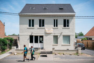 Wit gebouw van de stekerij met twee wandelaars vooraan